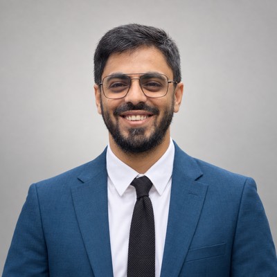 Faraz Khan in a blue suit and glasses, smiling